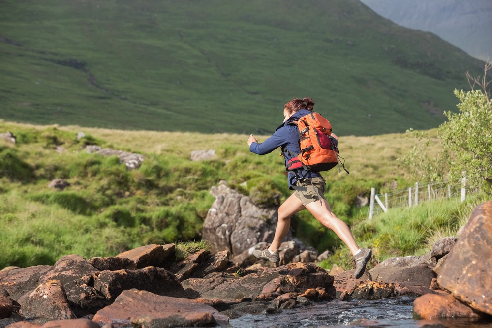 Athletic hiker leaping across rocks in a river in the countryside