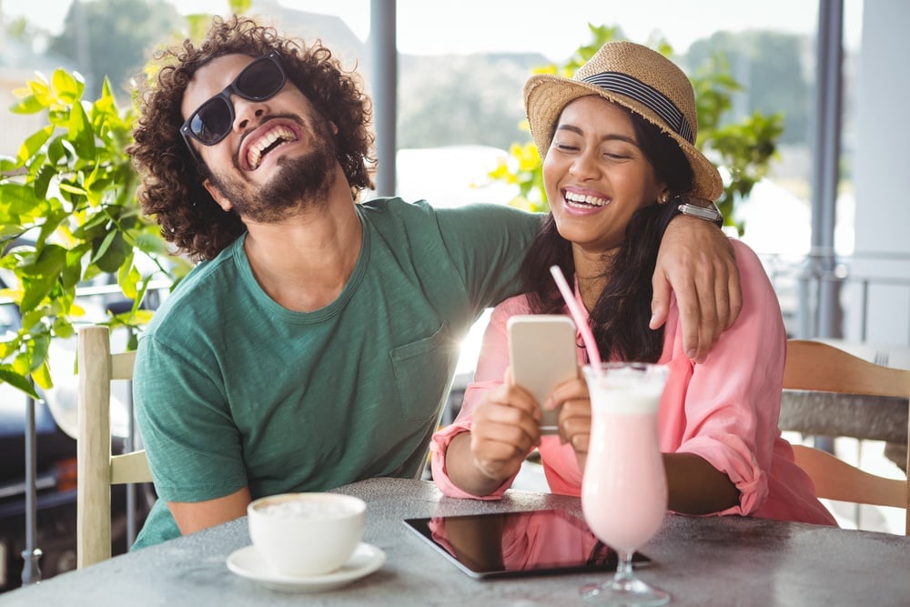 Couple having fun while using mobile phone in cafeteria