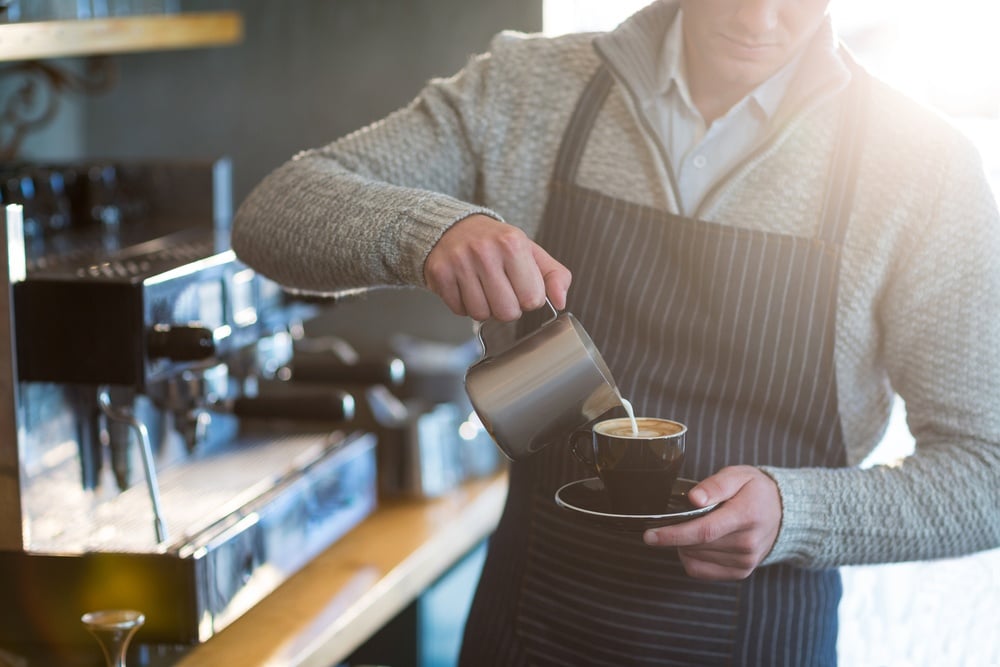Mid-section of waiter making cup of coffee at counter in cafe